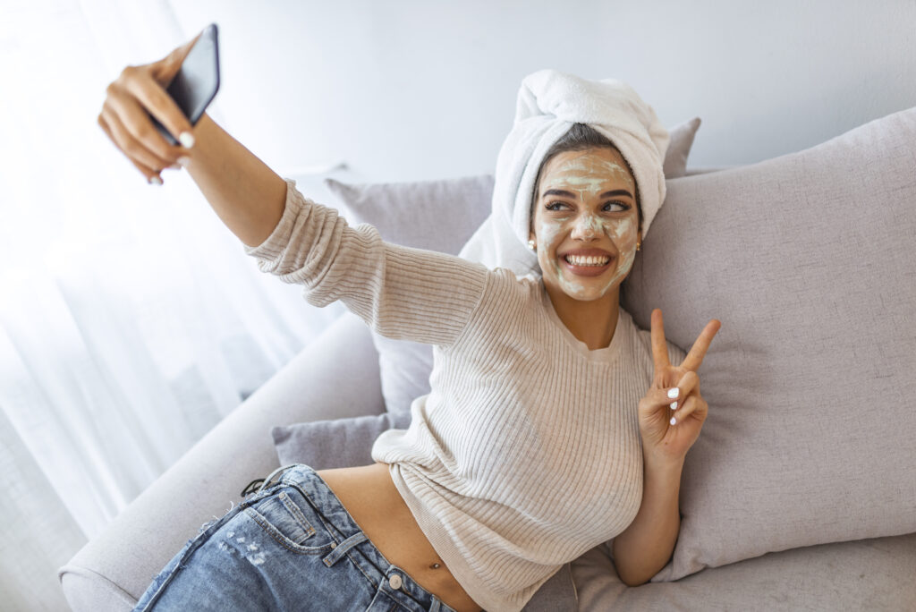 iStock 1162121236 1024x684 - Woman with clay mask taking selfie with mobile phone at home enjoying relaxation -